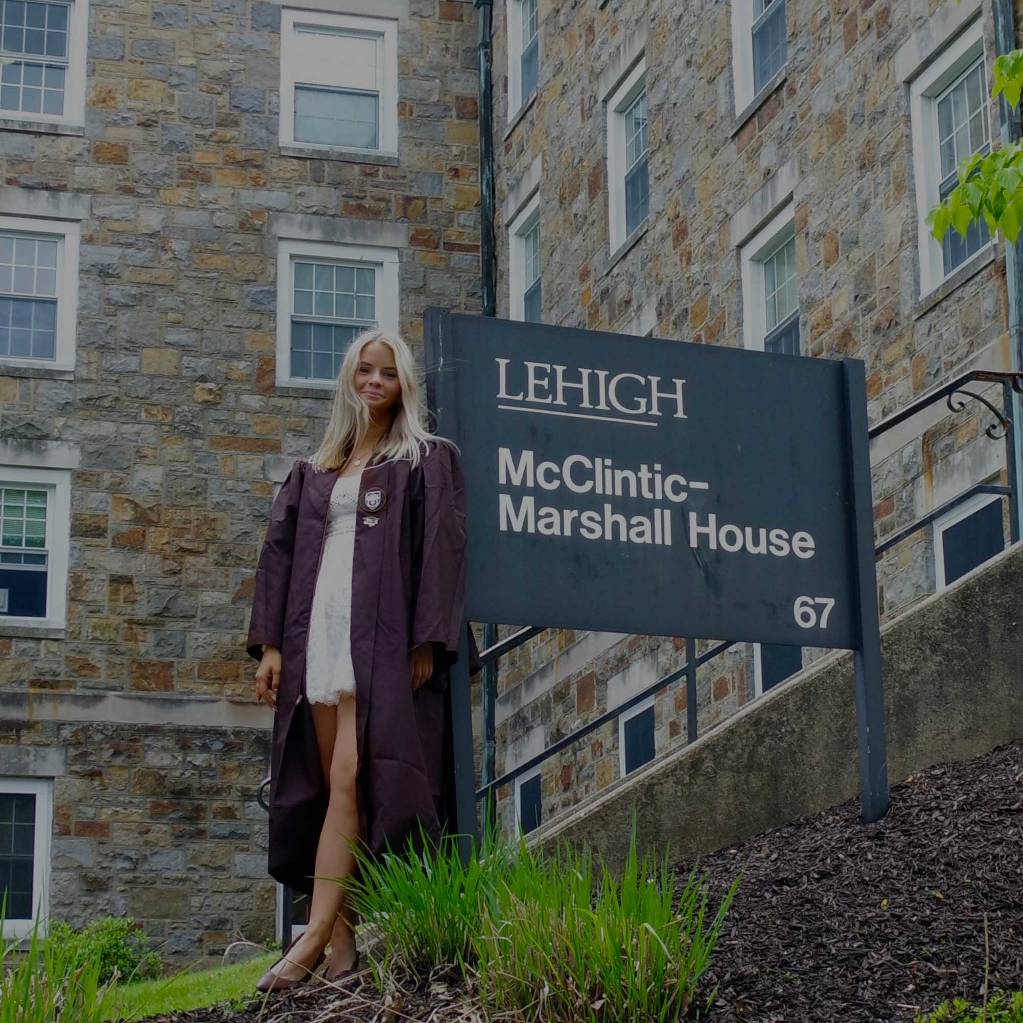 Caitlyn wears her graduation gown over a white dress and stands next to the McClintic-Marshall House sign.