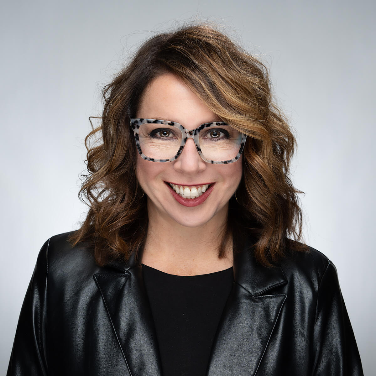 Carol Packard headshot, facing camera and wearing gray framed glasses against a gray backdrop.