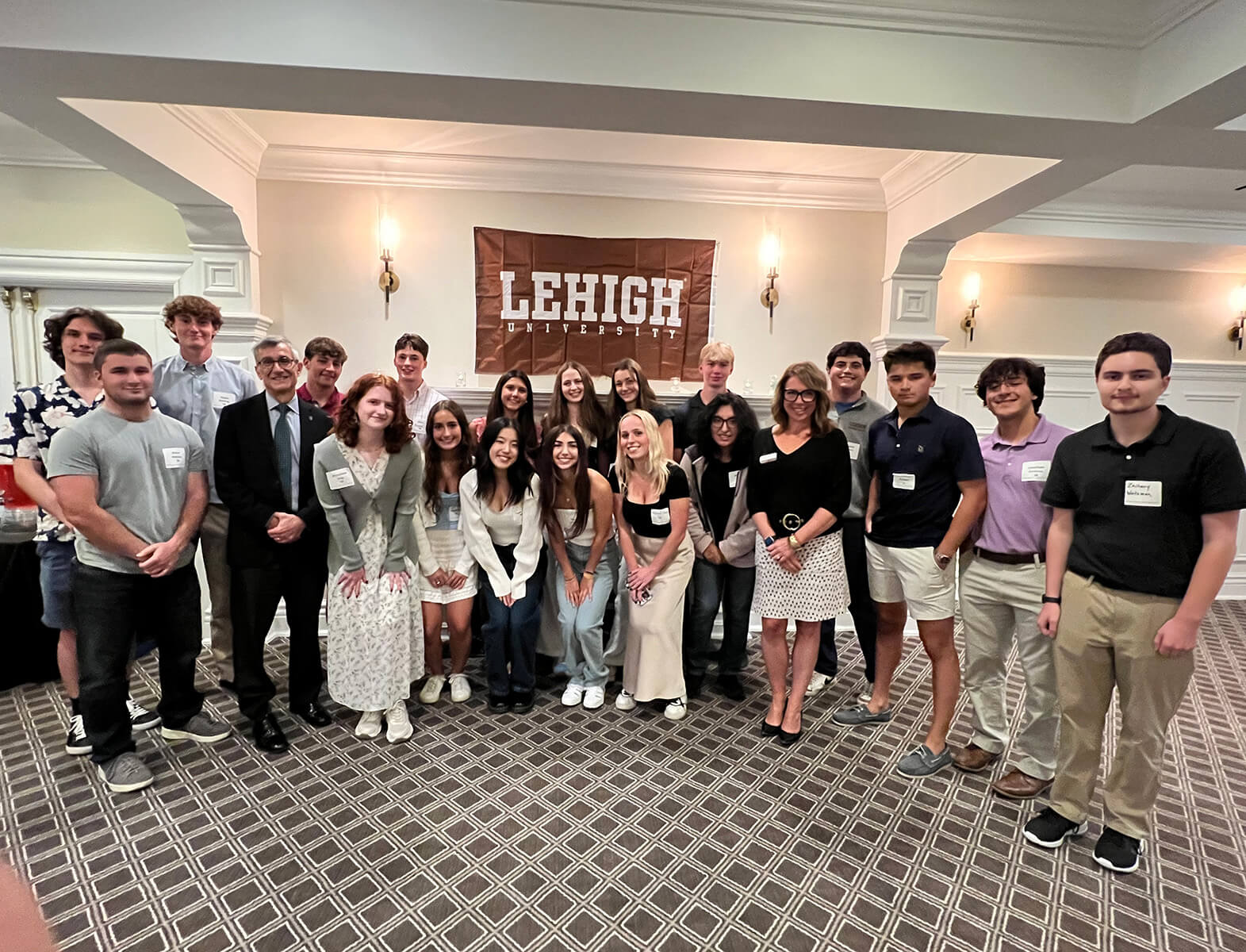 Carol Packard stands with a group of students and Joe Helble with a Lehigh banner handing in the background.