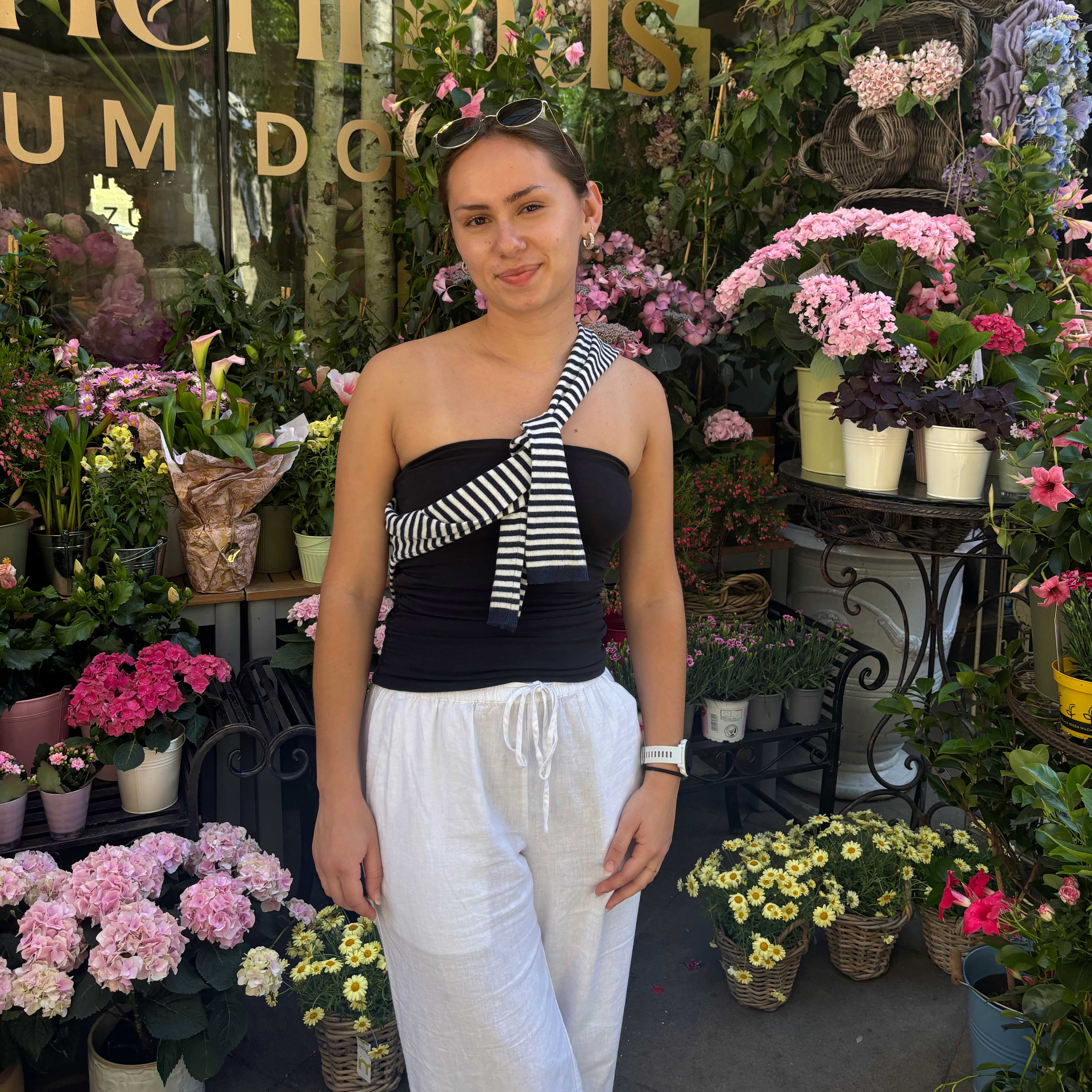 Charlotte stands outside of a shop in Vienna, Austria amongst several bright, potted flowers.