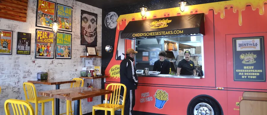 The inside of a restaurant where two men in a red food truck take the order of another man.