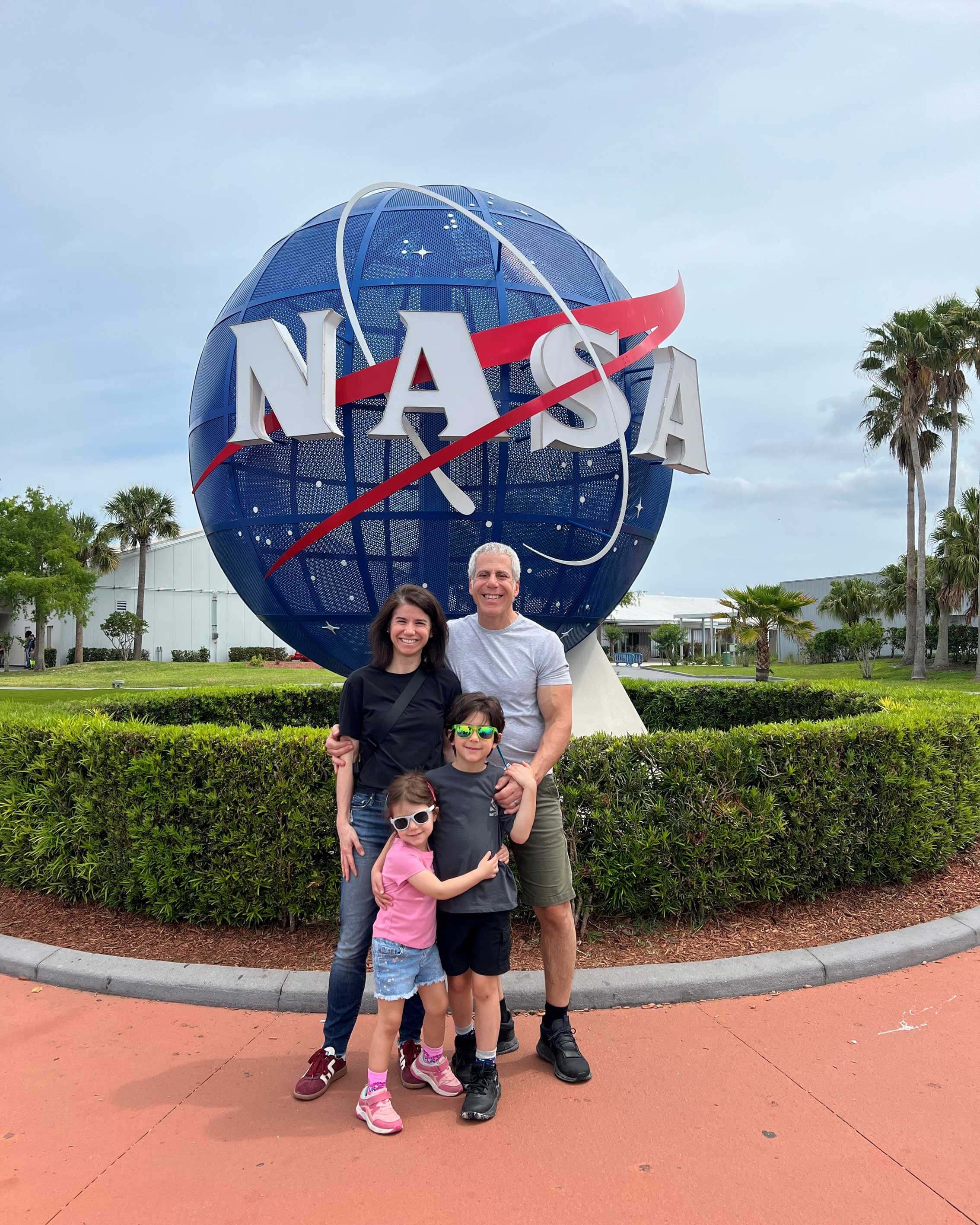 Christina, her husband, and her two children stand in front of the NASA insignia sphere in Florida.