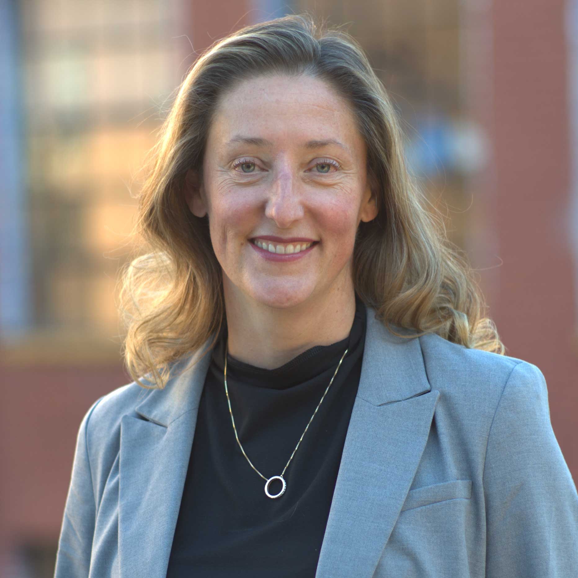 Christine smiles while wearing a light gray blazer, black shirt, and silver necklace.