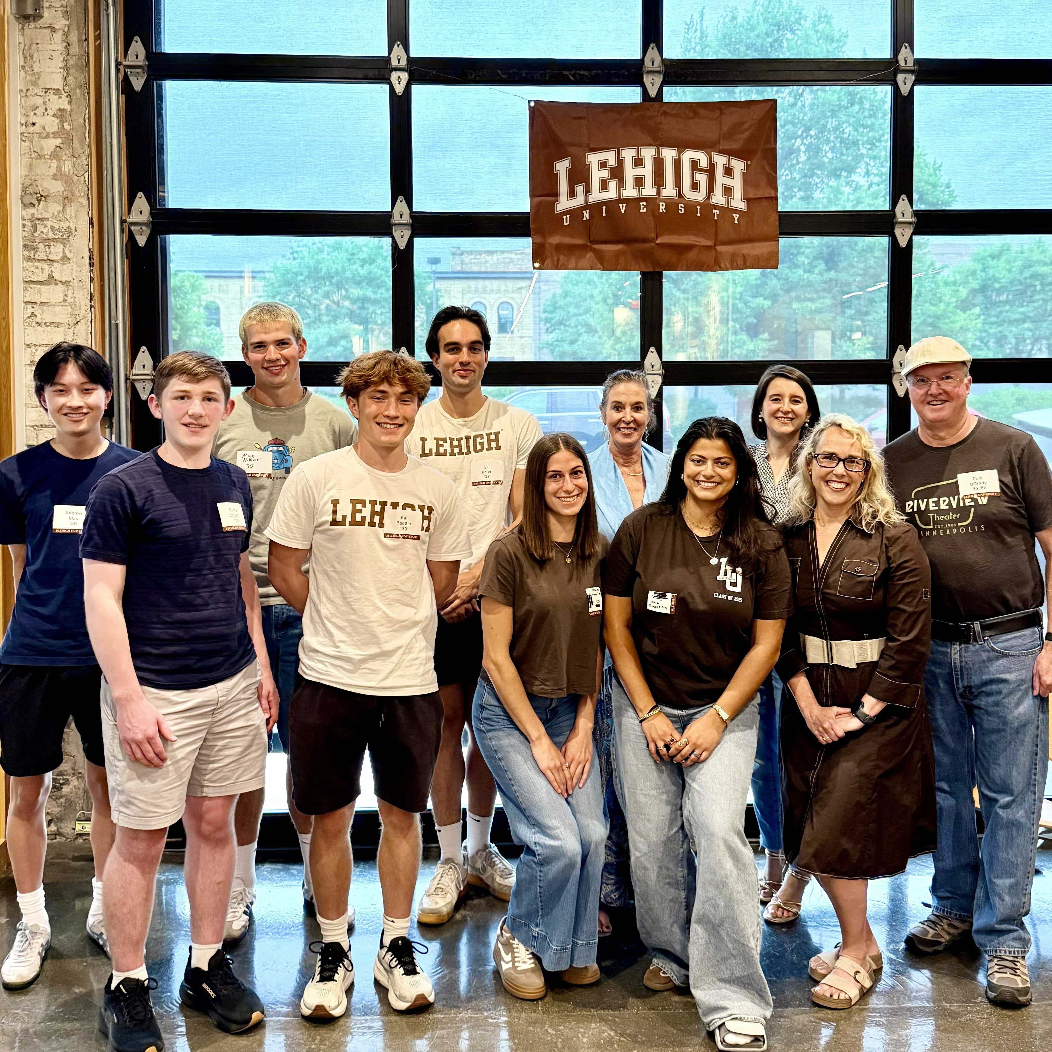 A group of students, alumni, and their families stand together and smile near a Lehigh banner. Christine stands with them.