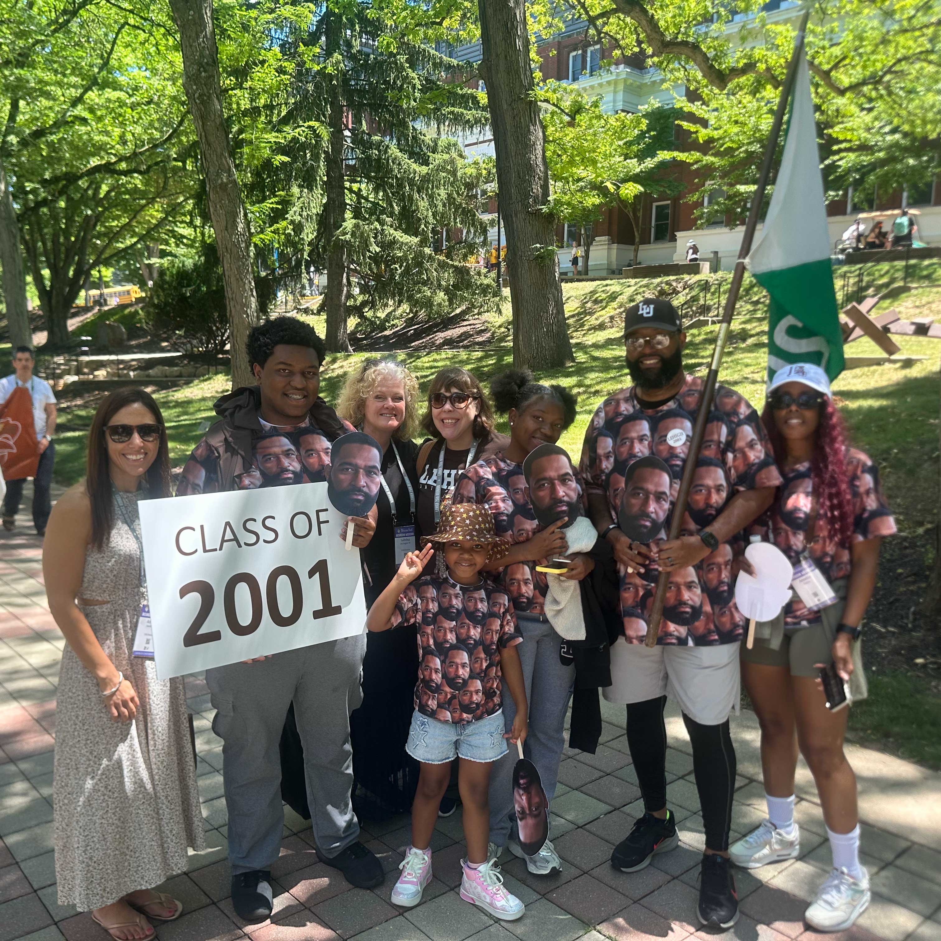 Members of the Class of 2001 pose with their class sign. A.D. and his family wear clothes printed with photos of his face on them.