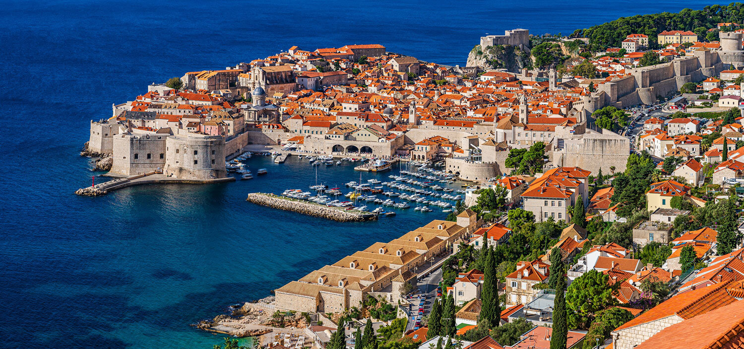 A port filled with boats and surrounded on three sides by white stone buildings capped with terracotta colored shingles.