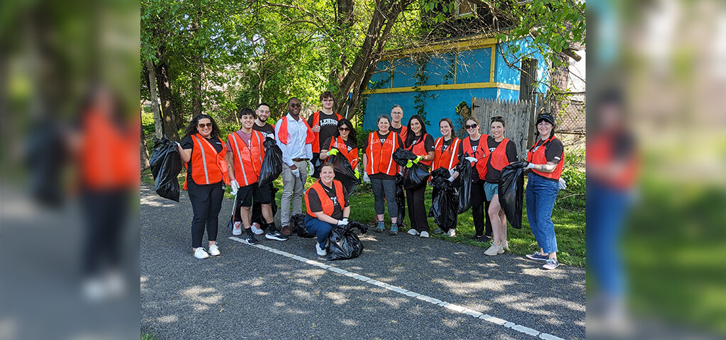 A group of volunteers wearing orange vests pose for a photo while carrying black trashbags.