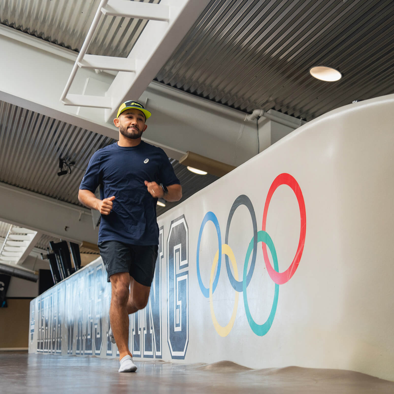 Darian Cruz runs along a wall in the gym that reads "Lehigh Wrestling" and shows the Olympic rings.