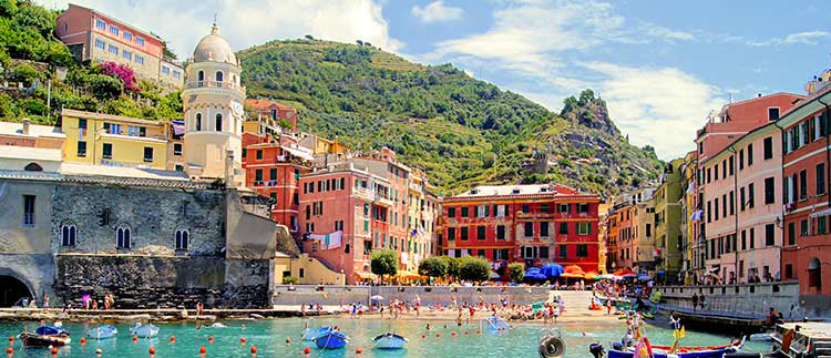 A Scenic view of Cinque Terre National Park beach with colorful old buildings against a backdrop of a green rugged mountain.