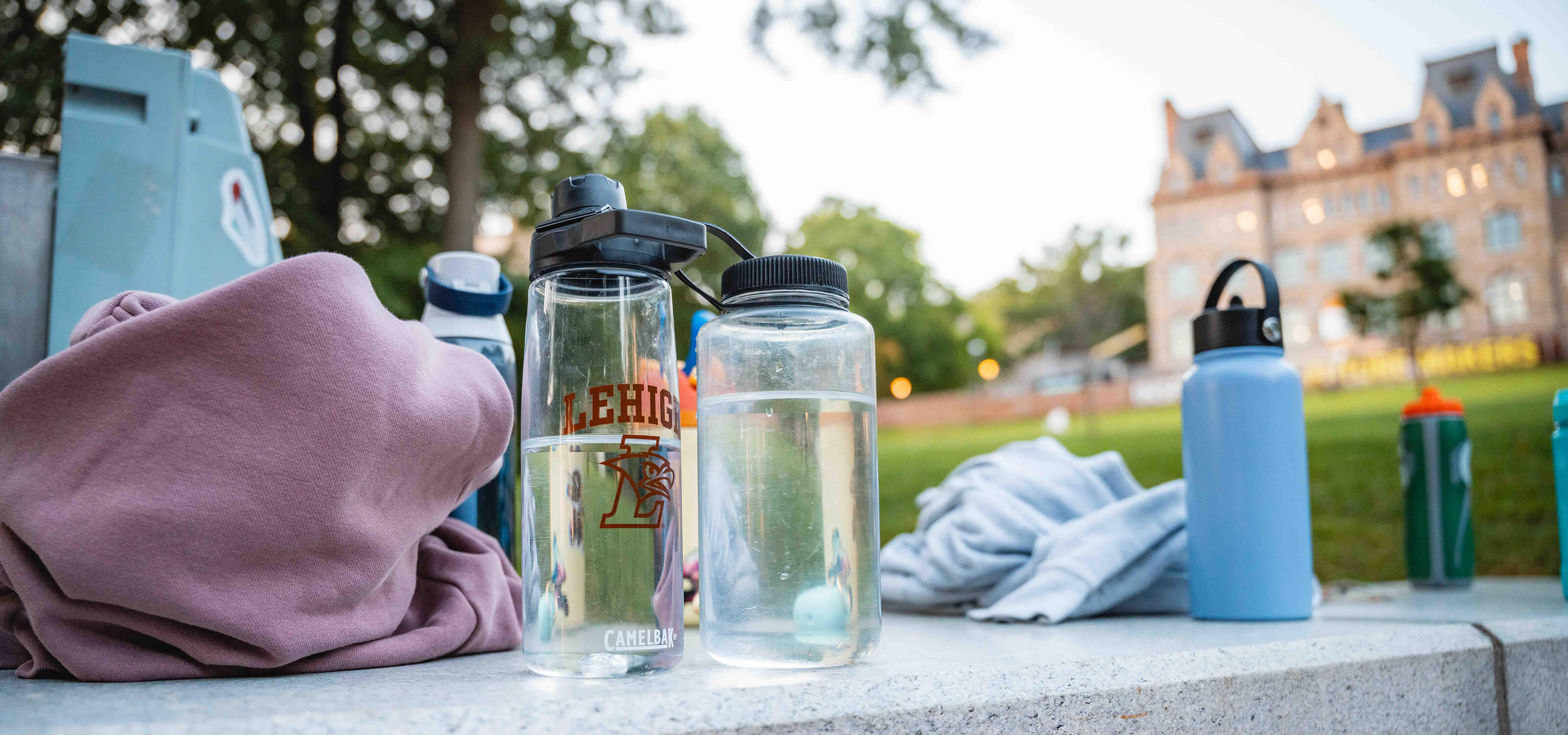 A variety of reusable water bottles sit on a stone wall with the university center in the background.