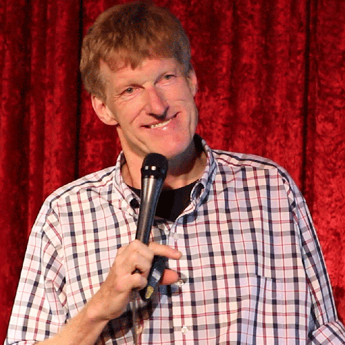 Don McMillan in plaid on stage holding a mic