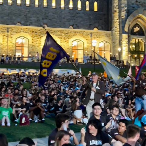 Doug walks through a crowd of students at their Rally. He waves the Class of 1980's blue and yellow flag.