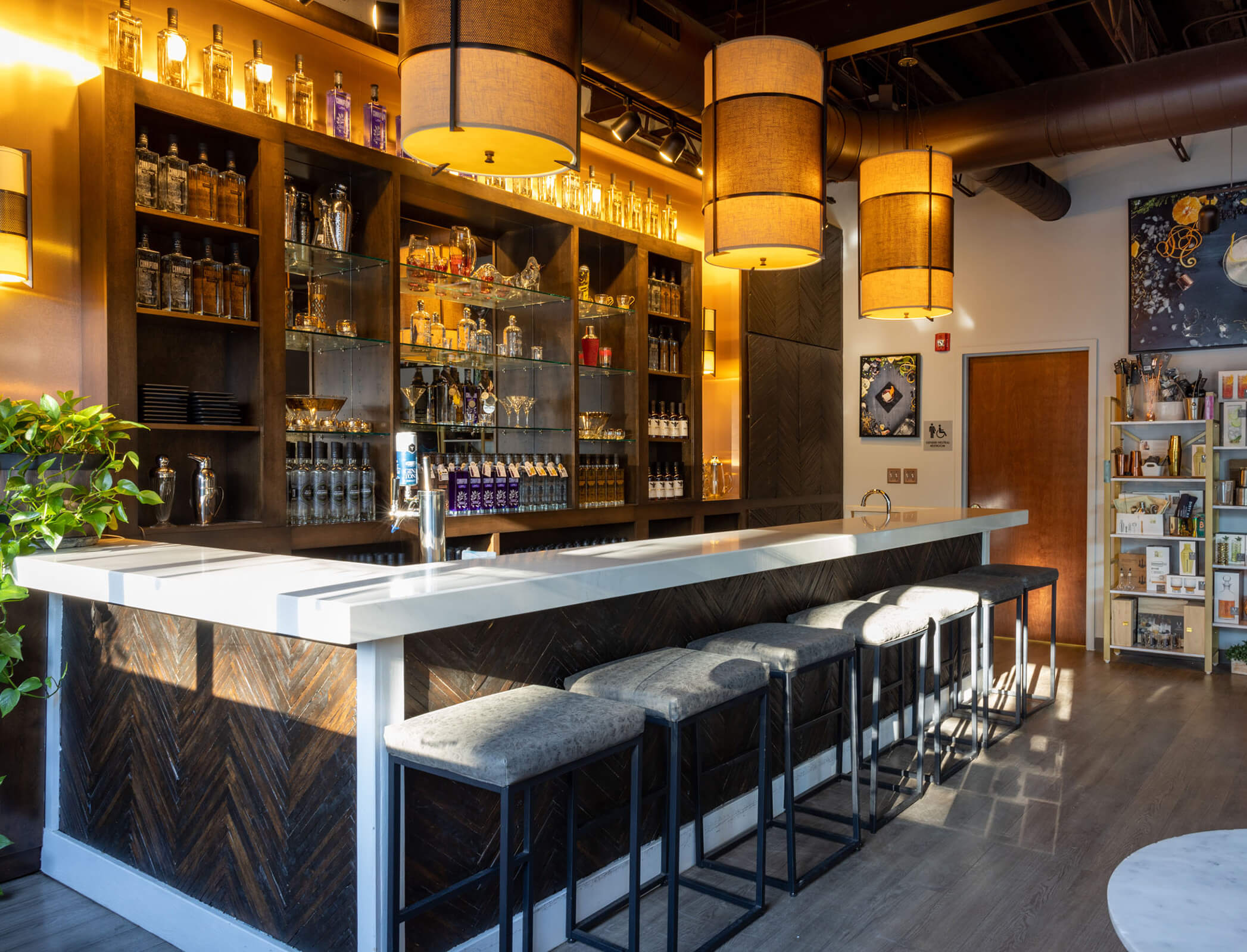 An intimate, warmly lit room with a white bar top and lit back bar featuring different bottles of liquor.