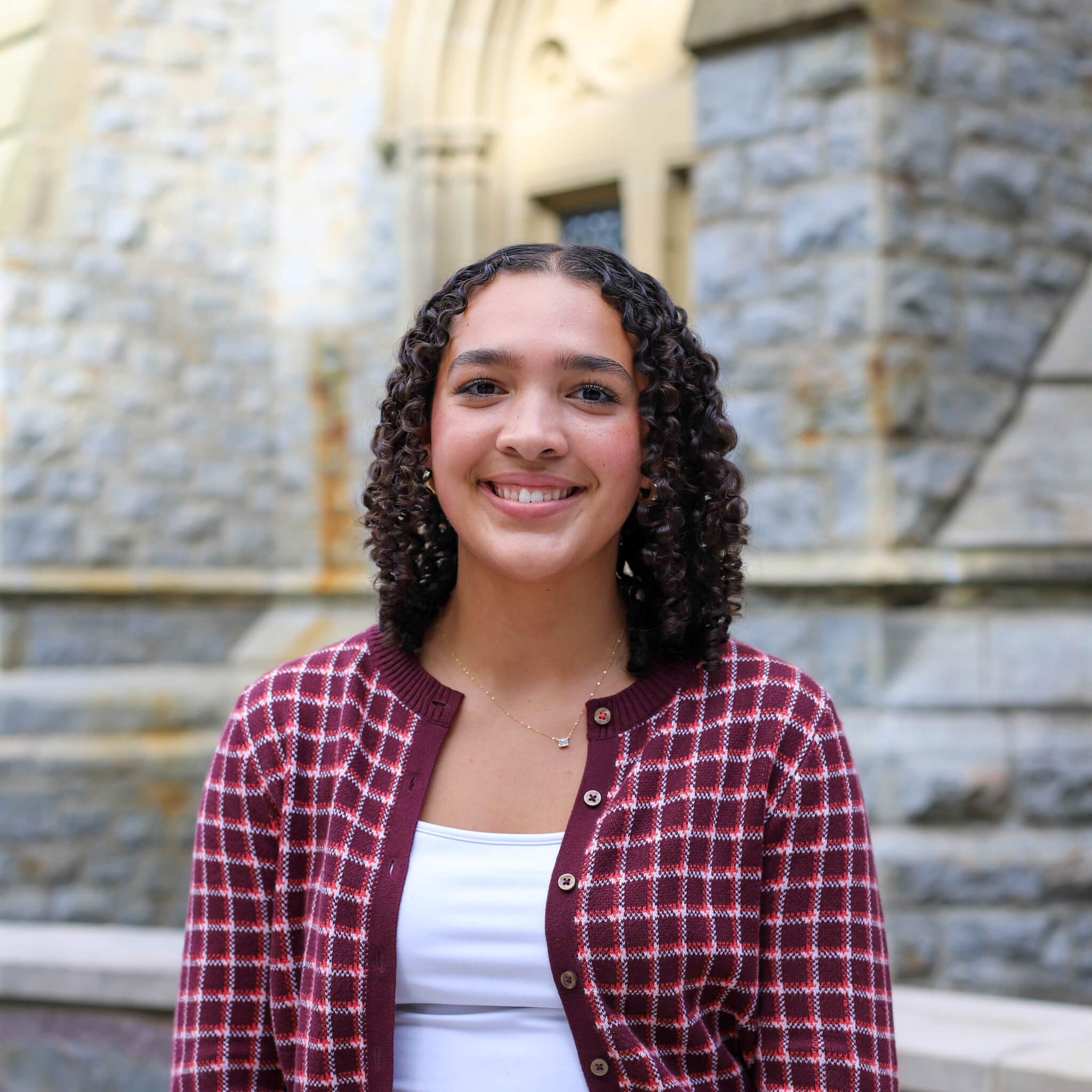 Emily wears a white camisole with a red and white striped sweater atop. The chapel building is visible behind her.