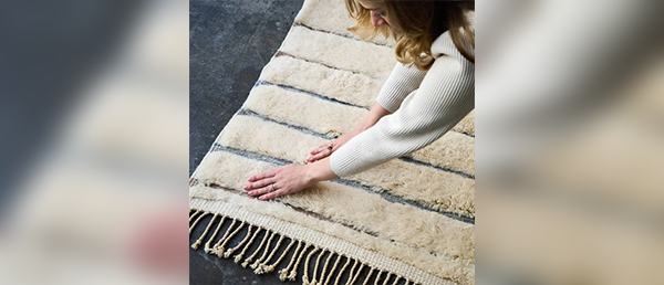 A close up of a woman adjusting a white textured rug with blue stripes.