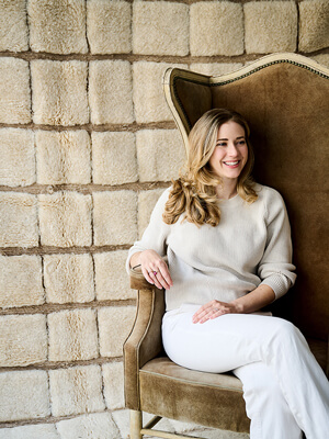 Erin Talgo sitting in a chair in from of a handcrafted lambswool rug