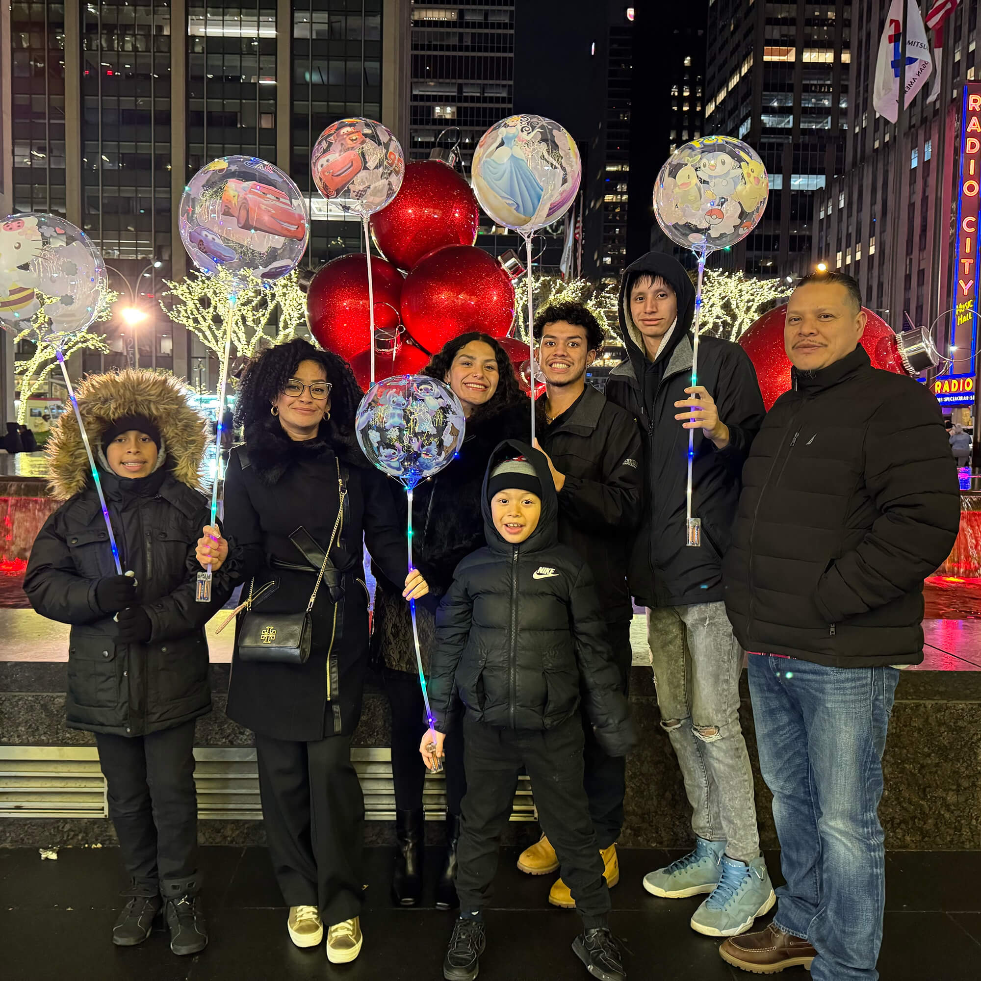 Standing outside Radio City Music Hall in New York City on a cold night, Arianna Morataya poses with her parents and four brothers, all holding balloons and wearing winter coats.