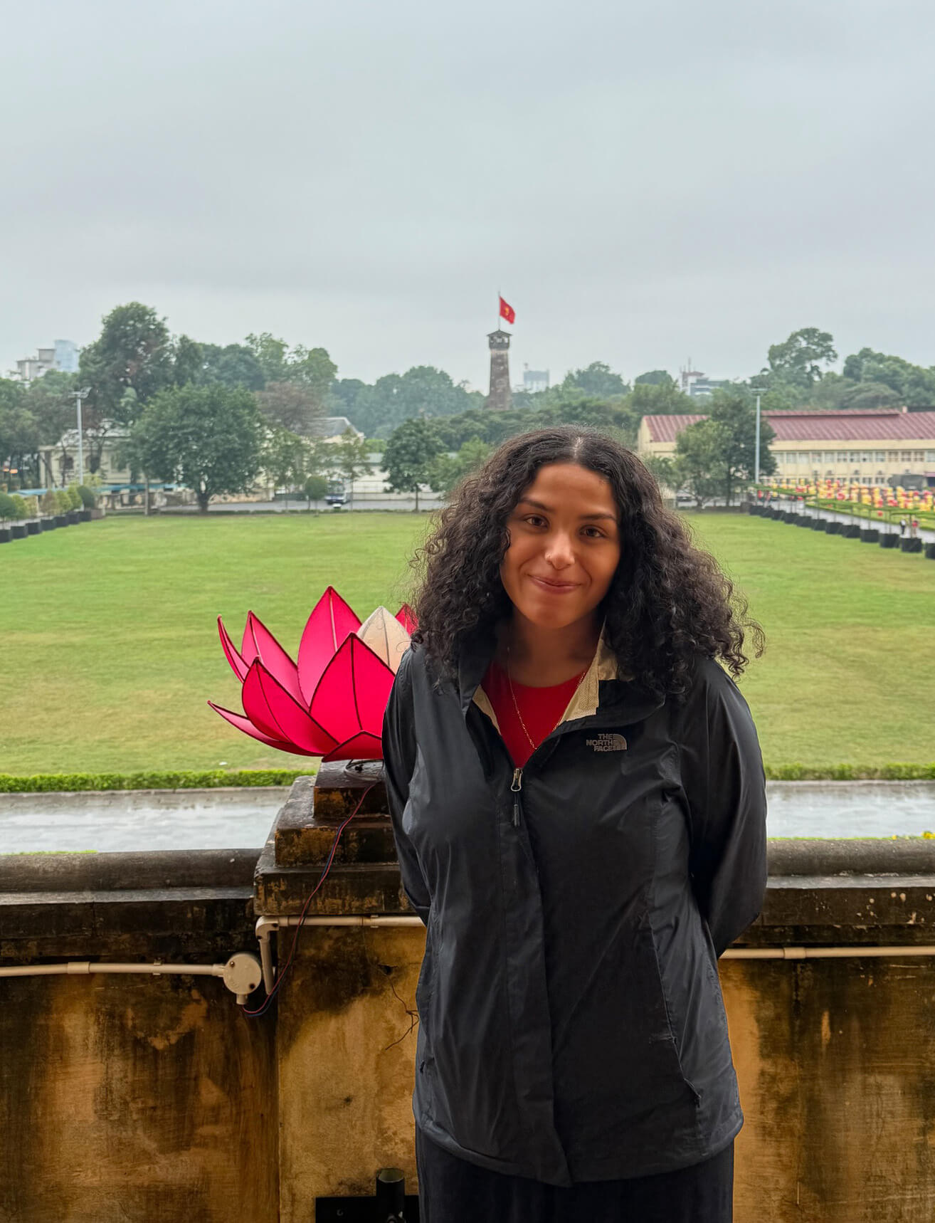Arianna Morataya stands on a balcony in Vietnam, overlooking a green lawn with a red flower sculpture behind her.