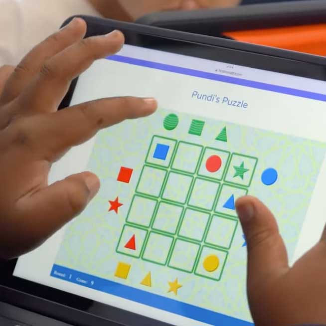 A child's hands holds a tablet and plays a puzzle.