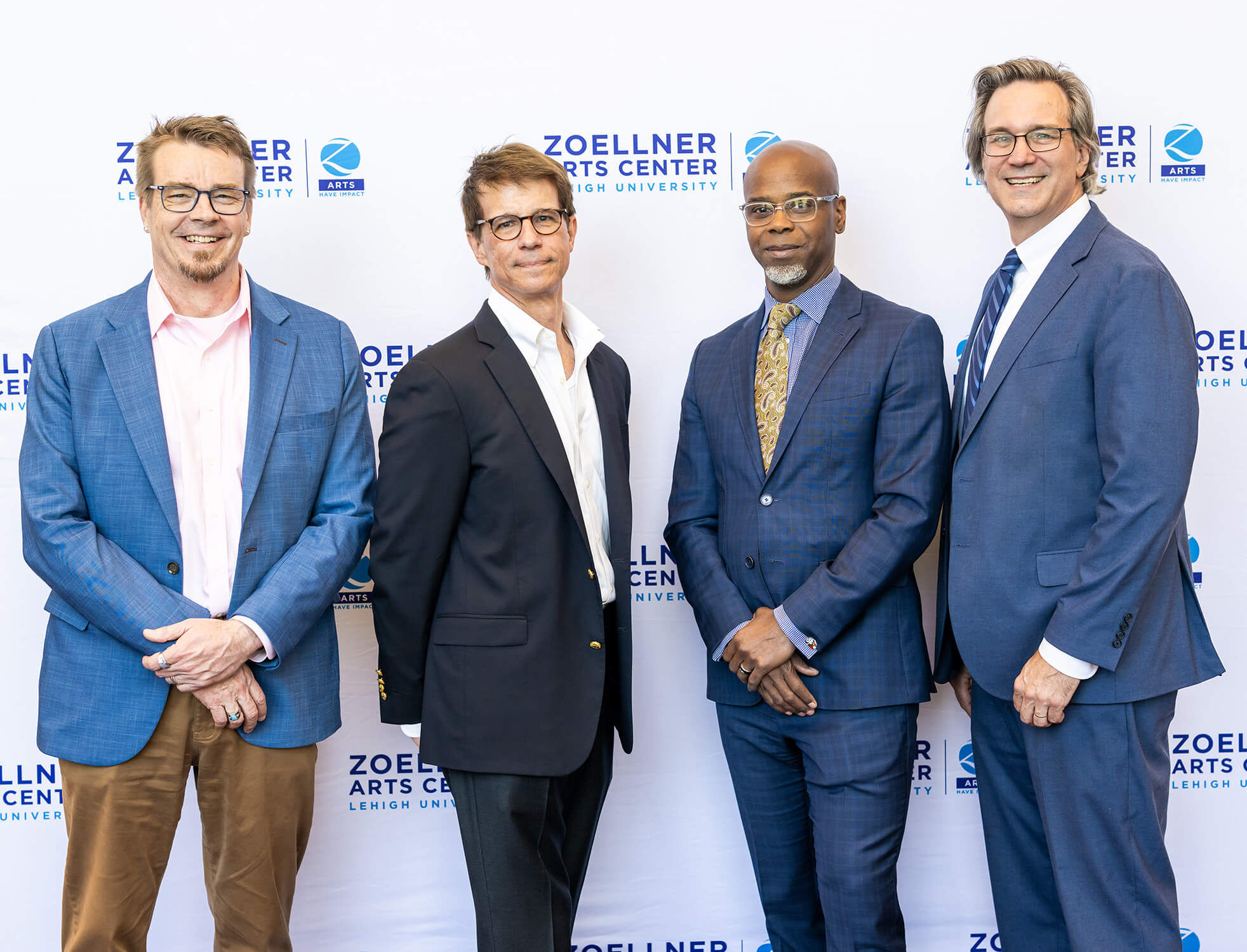 Dean Robert Flowers, Marc Falato, Mark Wilson, and Greg Reihman smile together in front of a “Zoellner Arts Center” step and repeat.