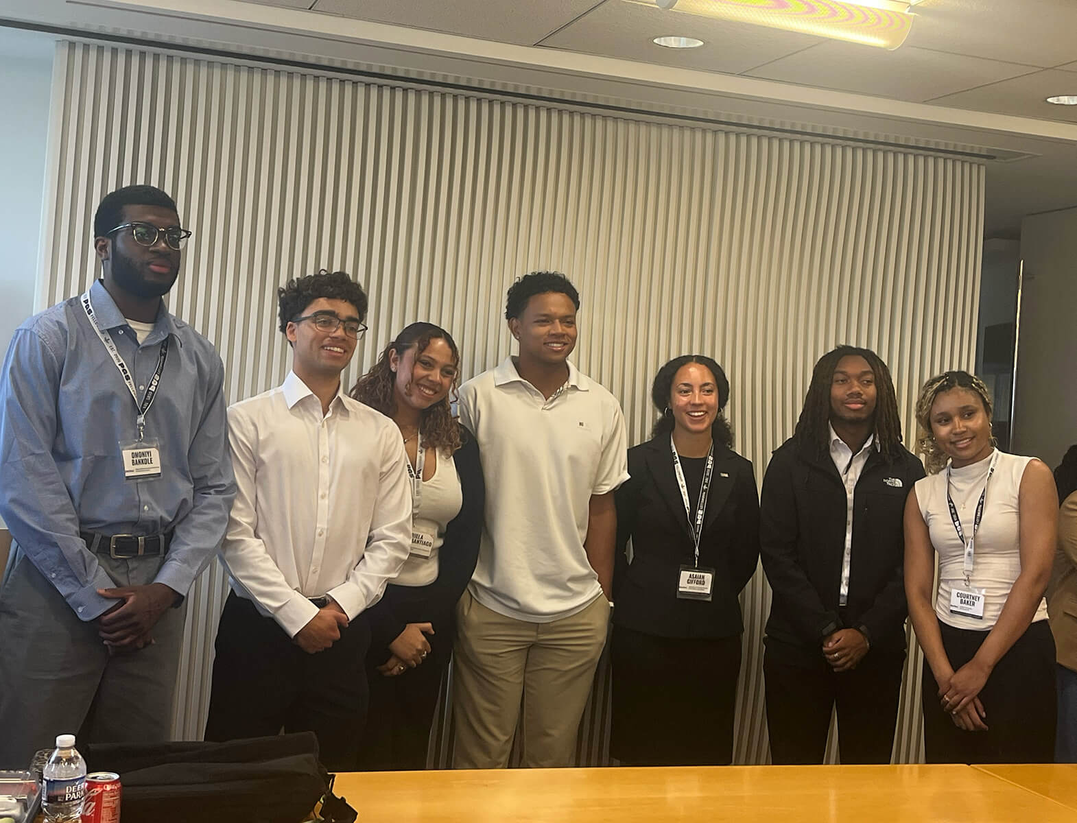 Courtney Baker, along with seven other fellows, stands in the front of a conference room wearing professional attire and smiling.