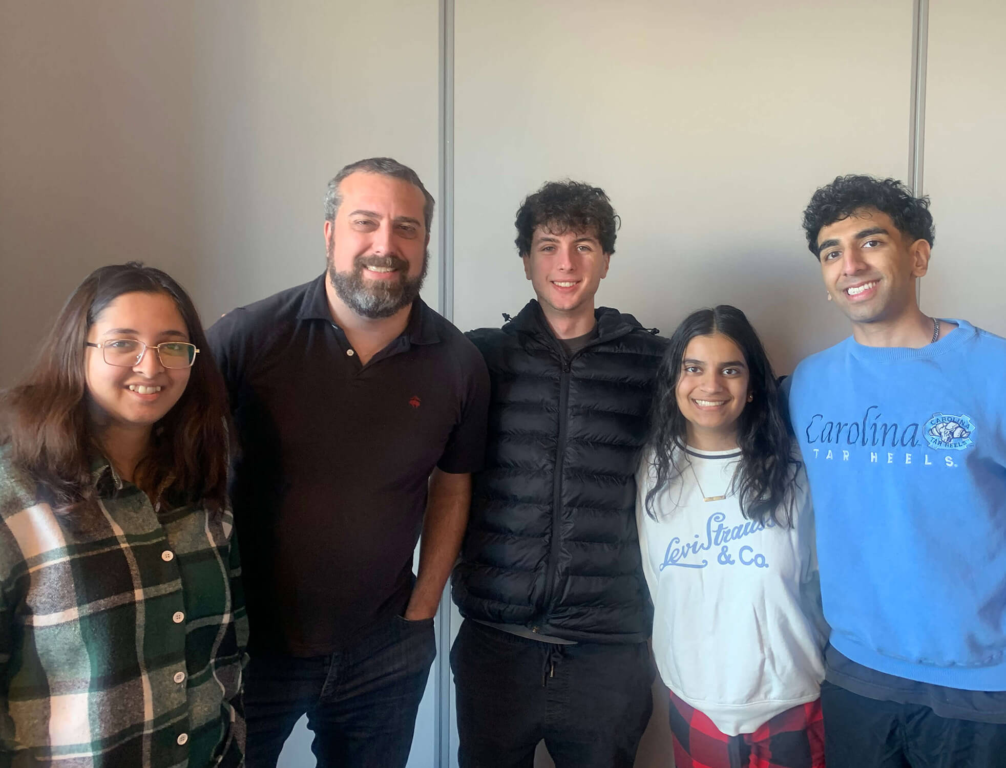 A group of five people pose for a photo wearing casual clothes and smiles.