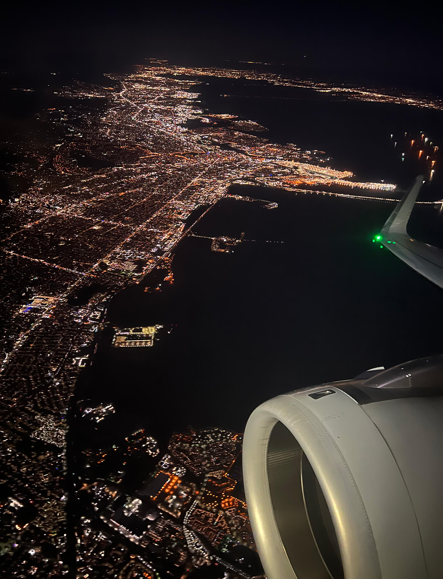 Aerial view of San Francisco at night from outside an airplane window, with an engine visible in the bottom right corner. 