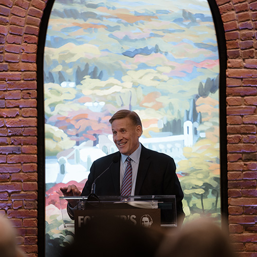 Kevin Clayton stands at a podium before a painted arch 