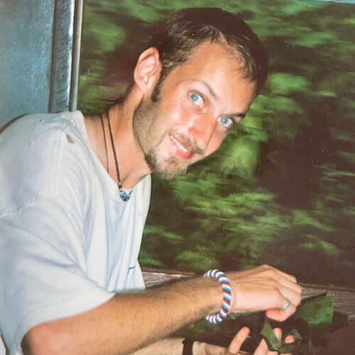 Franck Vogel looks up from his work to smile at the camera with the trees pictured as a blur outside his train window.