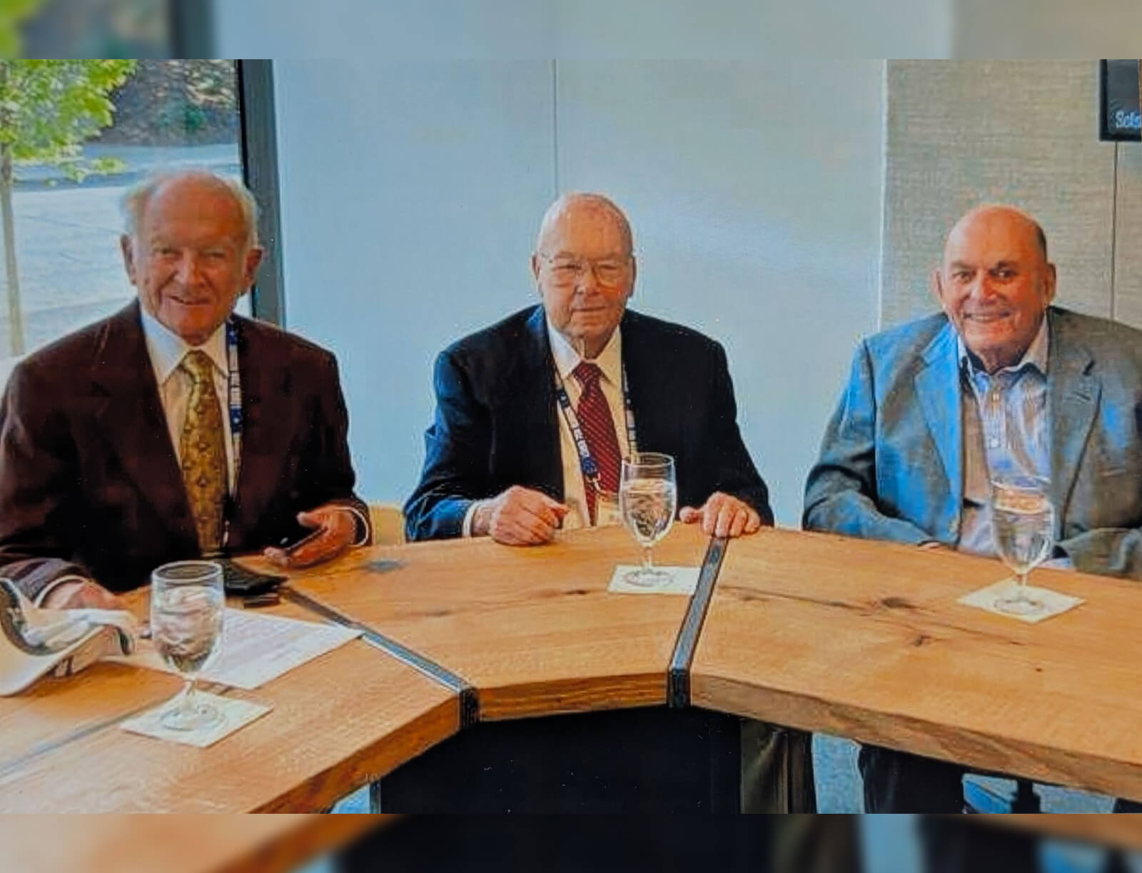 Herb Roemmele, Bob Gill, and Arthur Tauck Jr. sit at a table wearing suits and ties with glasses of water in front of them.