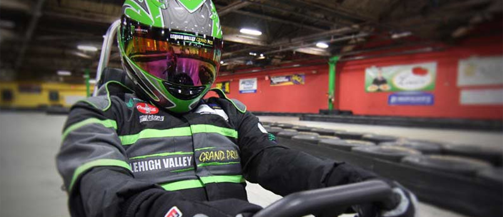 A close up of a go-kart driver in a black and green helmet and racing jacket.