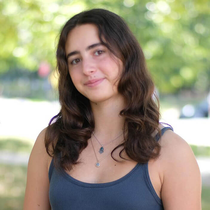 Hannah Null poses with a closed mouth smirk for an outdoor headshot with green foliage in the background.