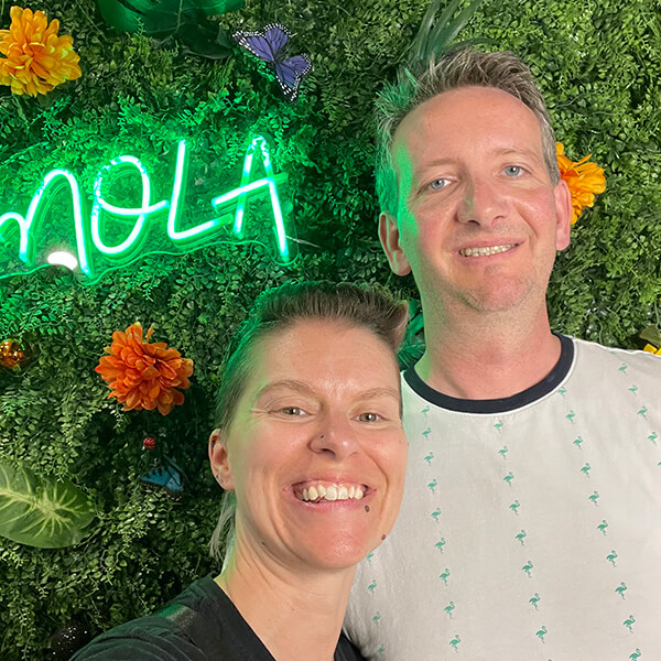 Megan and Travis Hannan smiling in front of NOLA neon sign