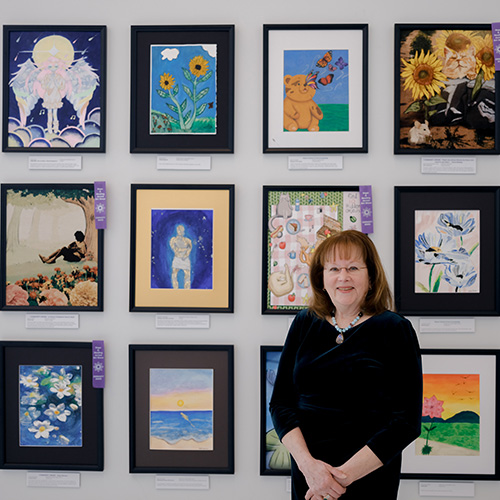 Heather Rodale '74 stands in front of three rows of student created art