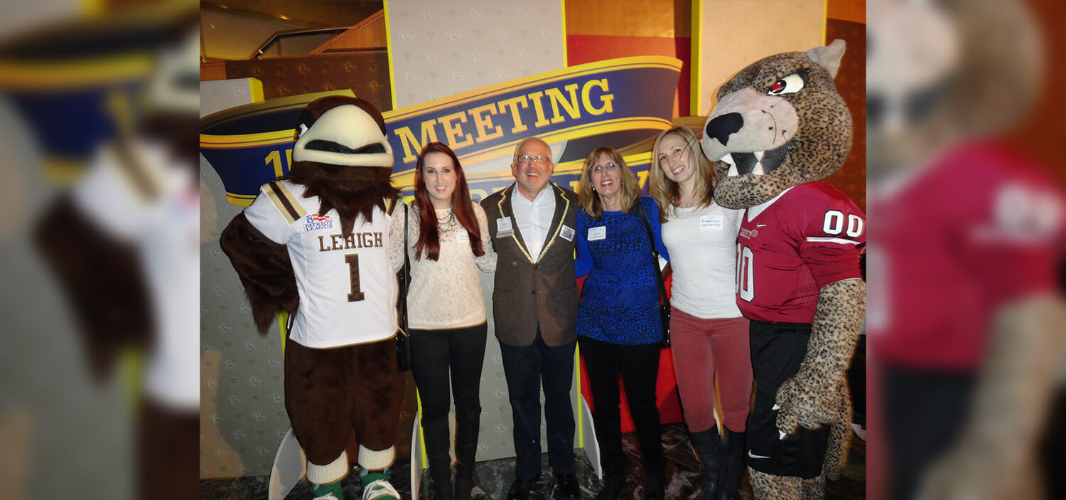 A family of four smile standing between the Lehigh Mountain Hawk mascot and the Lafayette Leopard mascot