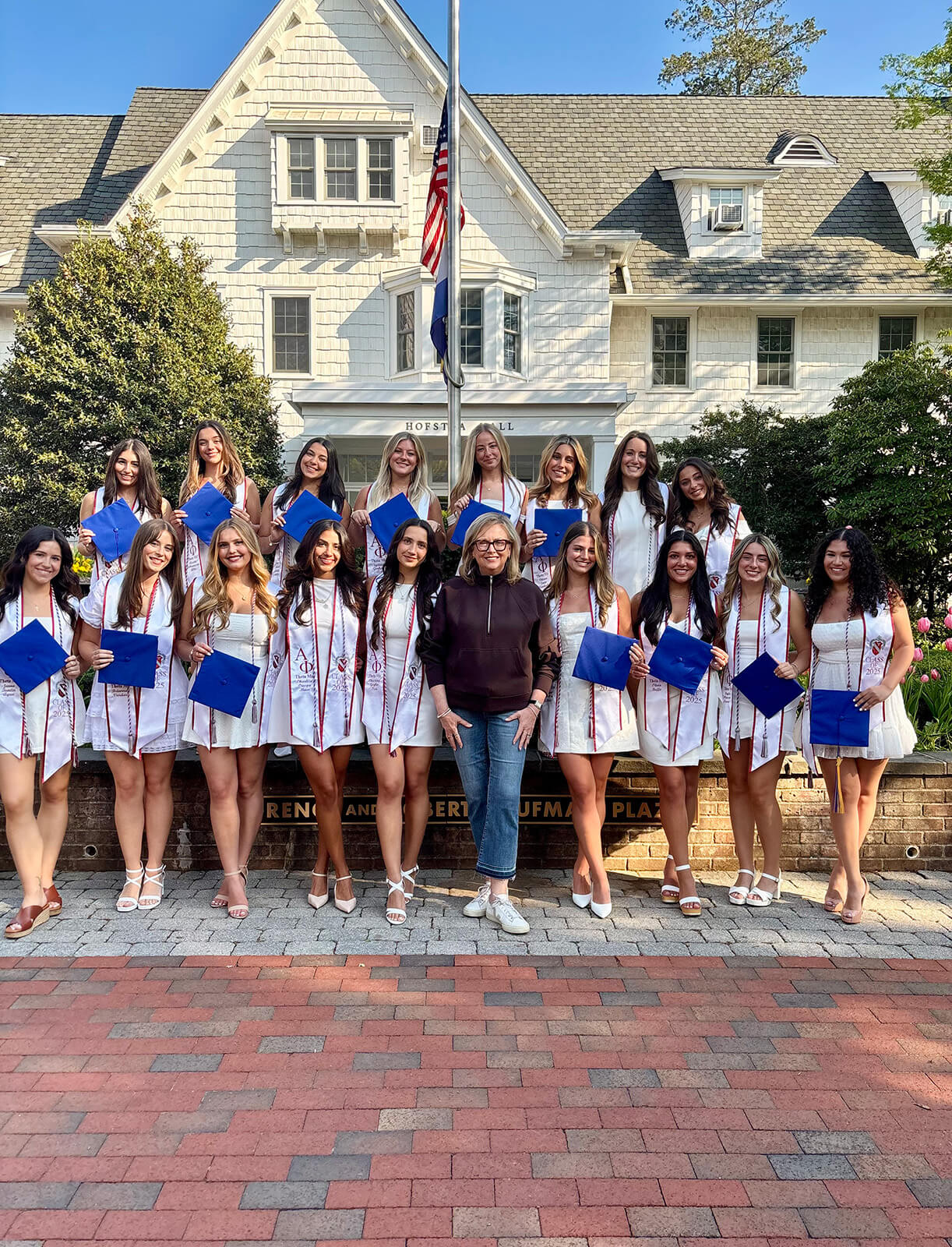 Mary Beth Tully stands center among the graduating class of women, all wearing white dresses and holding blue graduation caps.