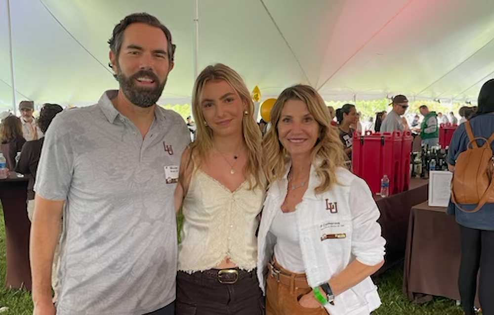 A family of three wearing brown and white Lehigh attire stand together for a family photo.