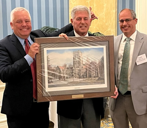 Three men in suits stand behind a framed painting of Alumni Memorial