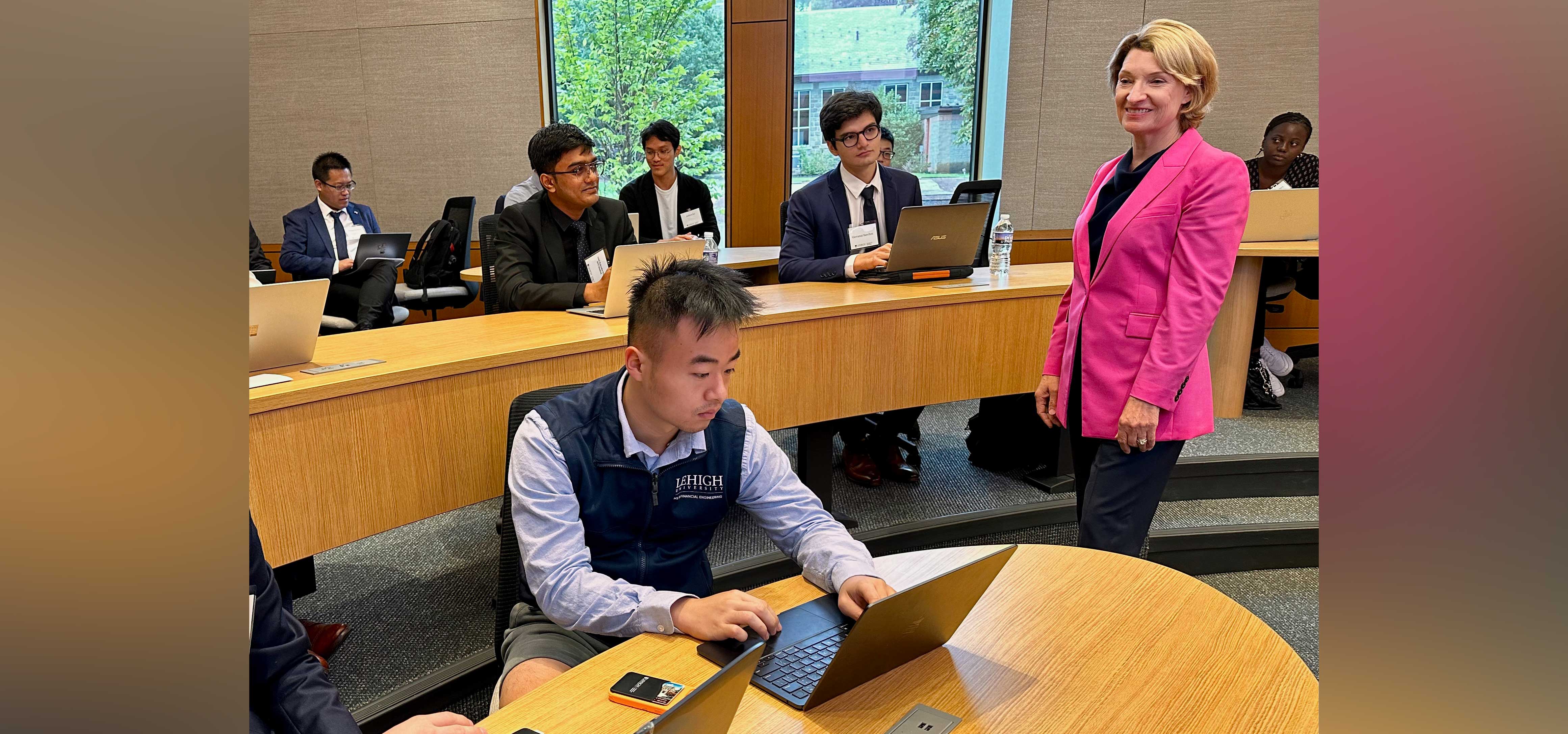 A professor smiles while walking around students on their laptops.
