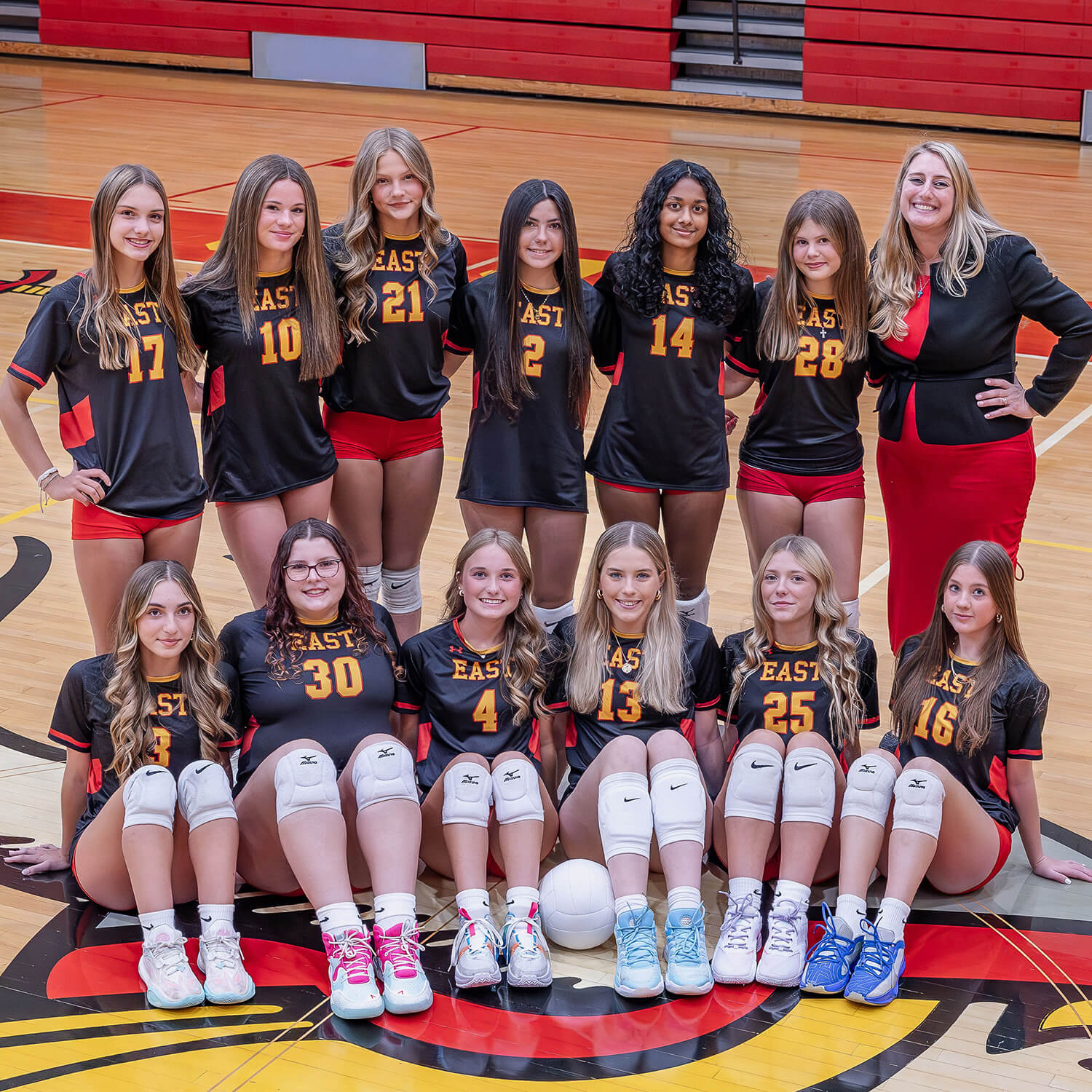 Rochelle Sheridan poses with a girls volleyball team on their home court, all wearing red and black.
