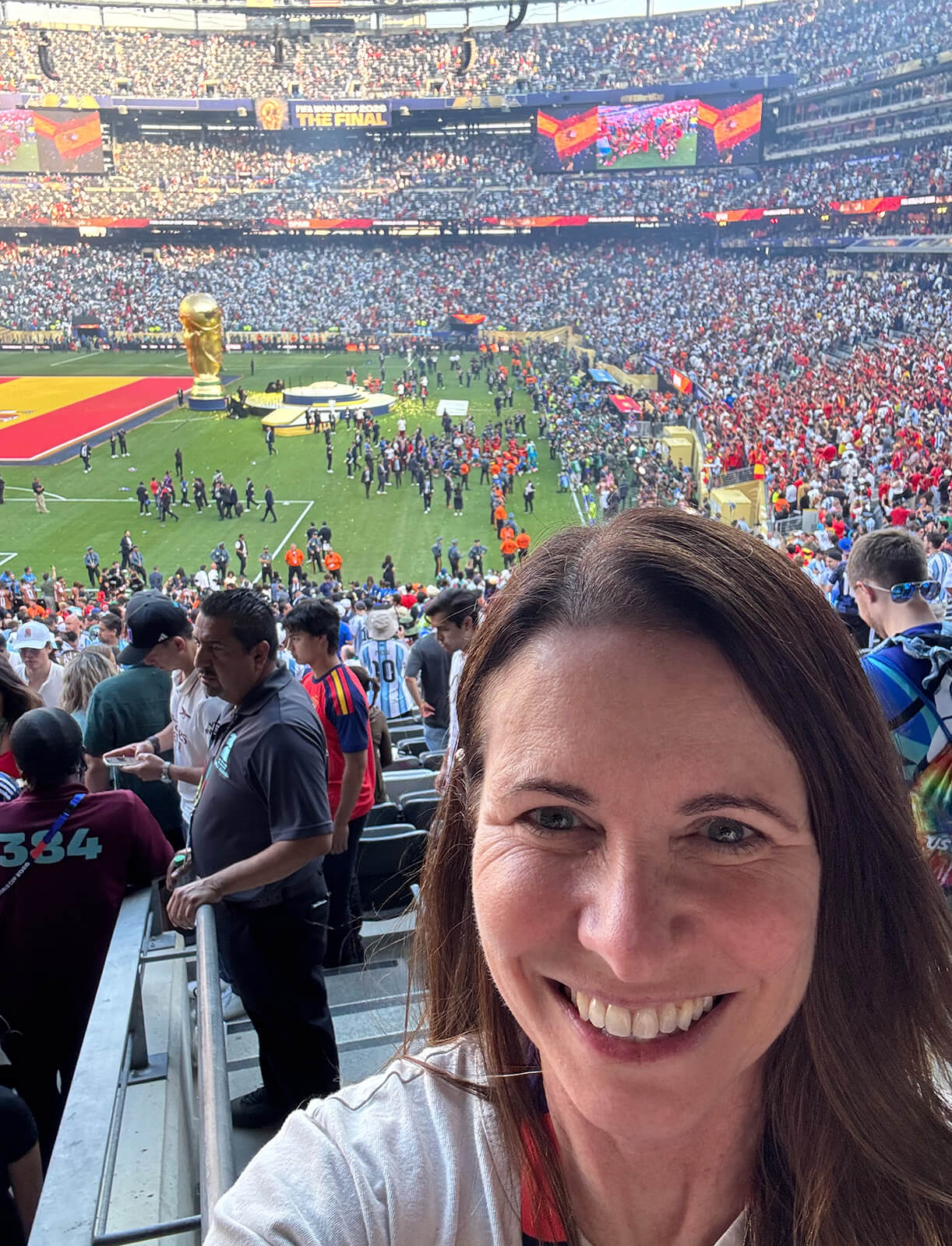Donna Providenti poses for a selfie in a crowded stadium with the World Cup stage set behind her.