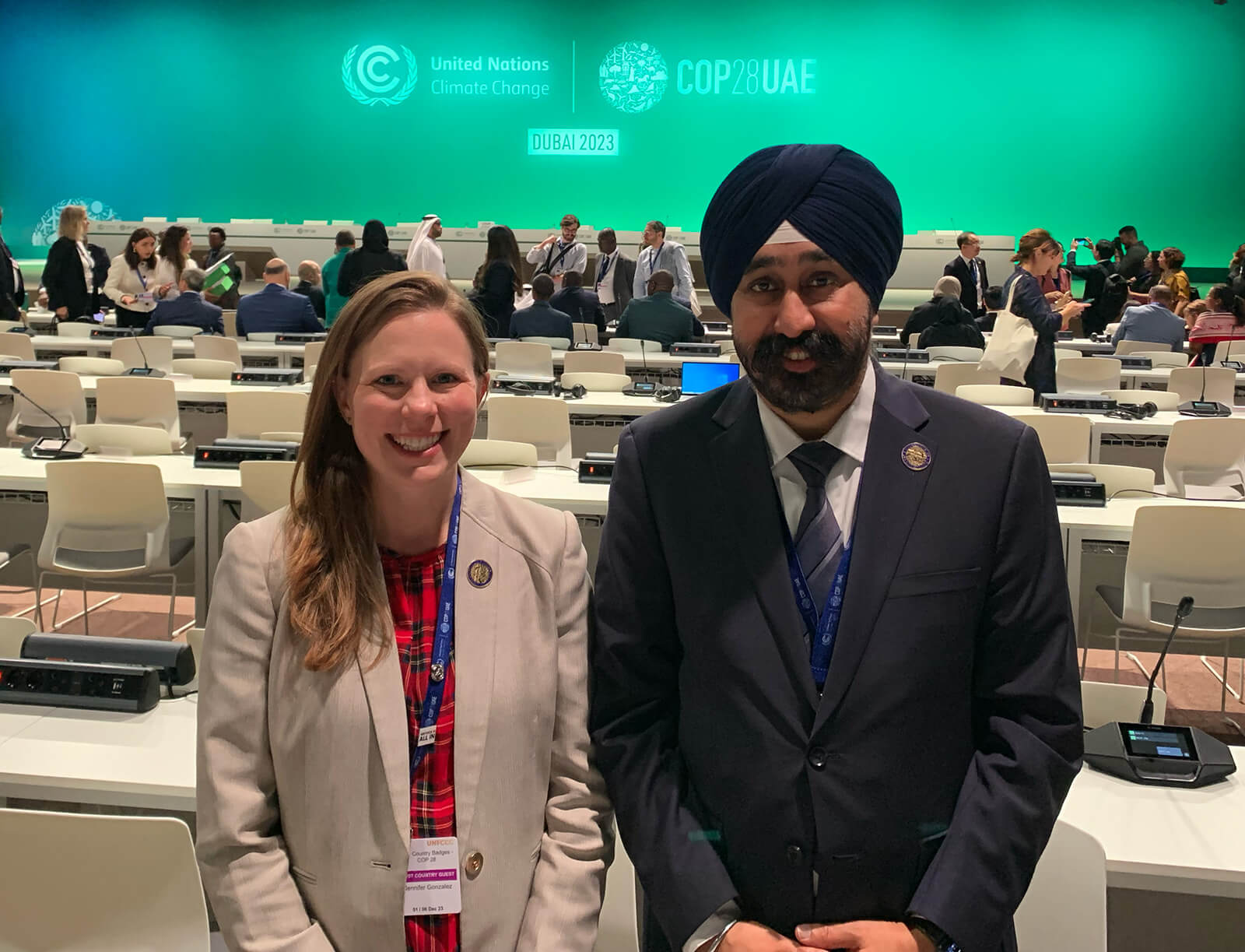 Jennifer Gonzalez stands with Mayor Ravi Bhalla at the UN Climate Change Conference, with conference tables facing a stage positioned behind them.