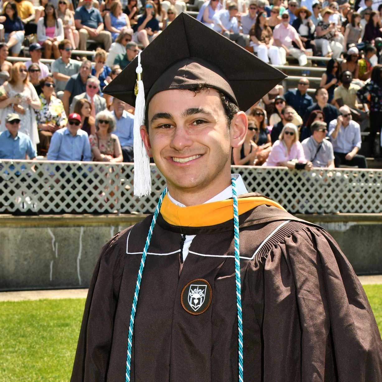Jake wears his cap and gown at graduation over a white collared shirt.