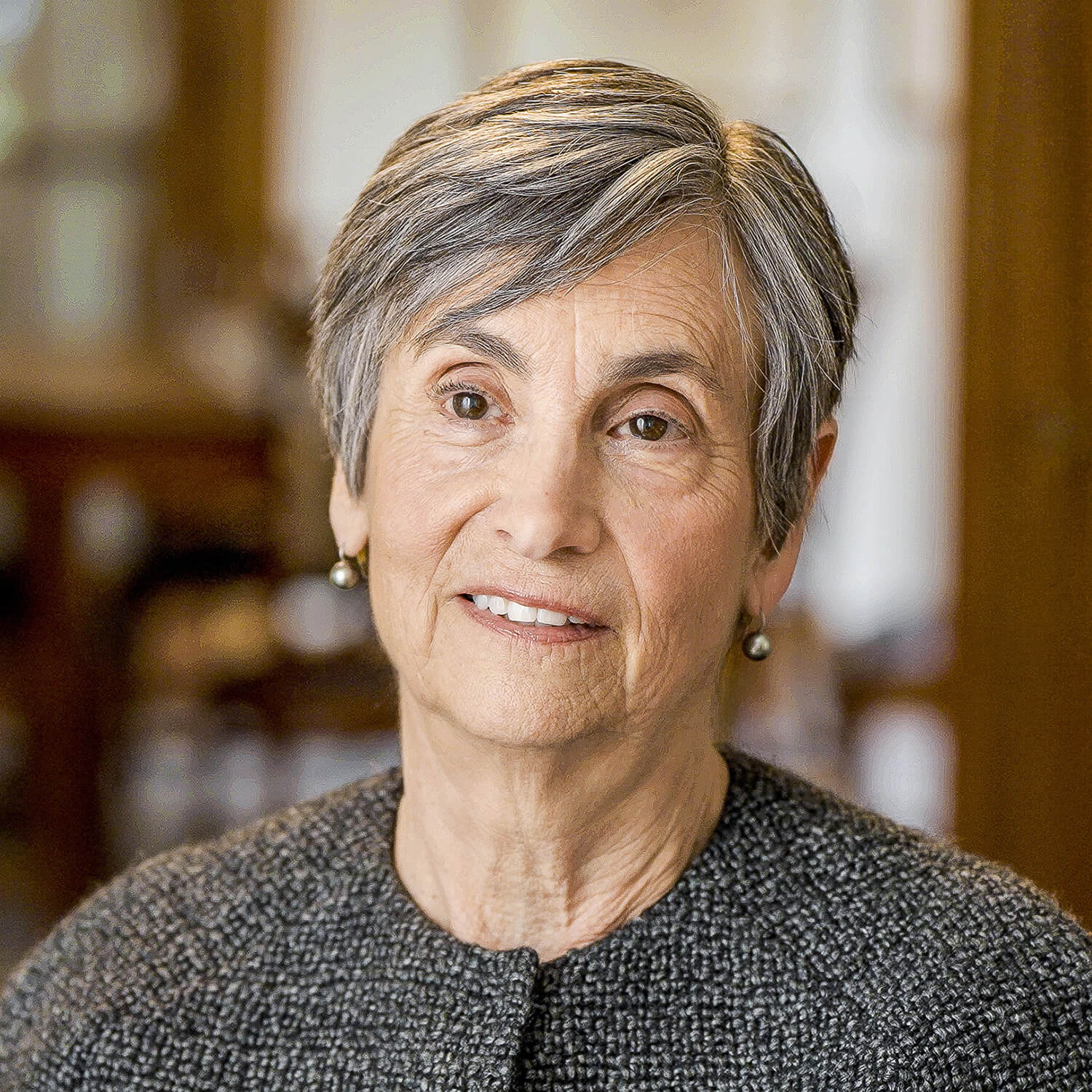 Jane Jamieson sits and looks off camera, wearing short hair and small silver drop earrings.