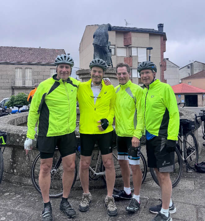 Jim Davis ’79, Lehigh University alumnus and former Colgate-Palmolive executive stands with 3 fellow alumni, all wearing neon yellow wind breaker jackets and gray helmets and posing in front of a statue with a bike. 