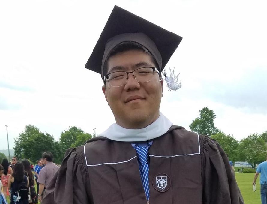 John Lim stands in his cap and gown at graduation