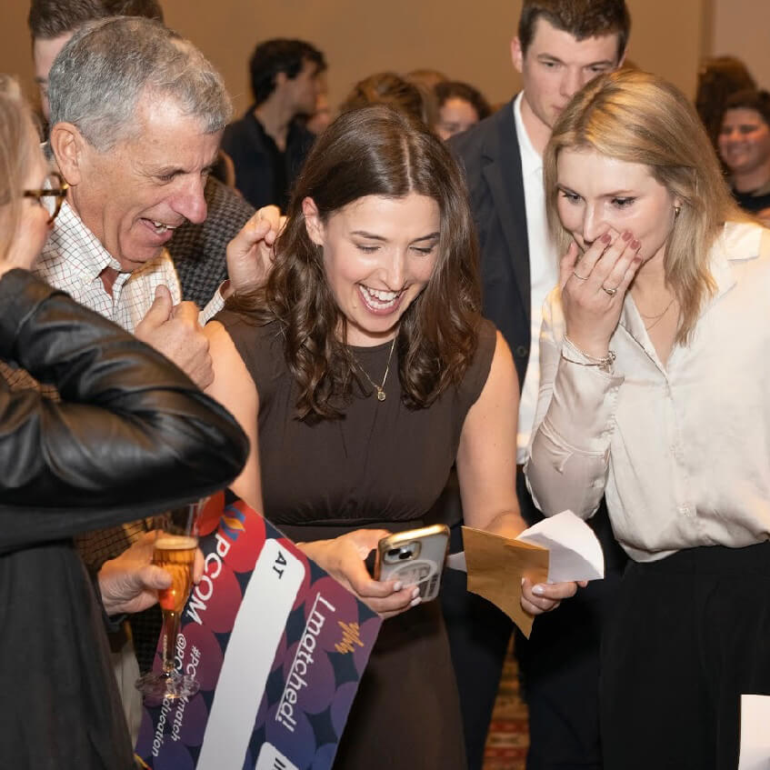 Julia and her family smile widely as they glance down at Julia's phone after getting word that Ali got into Yale as well. 