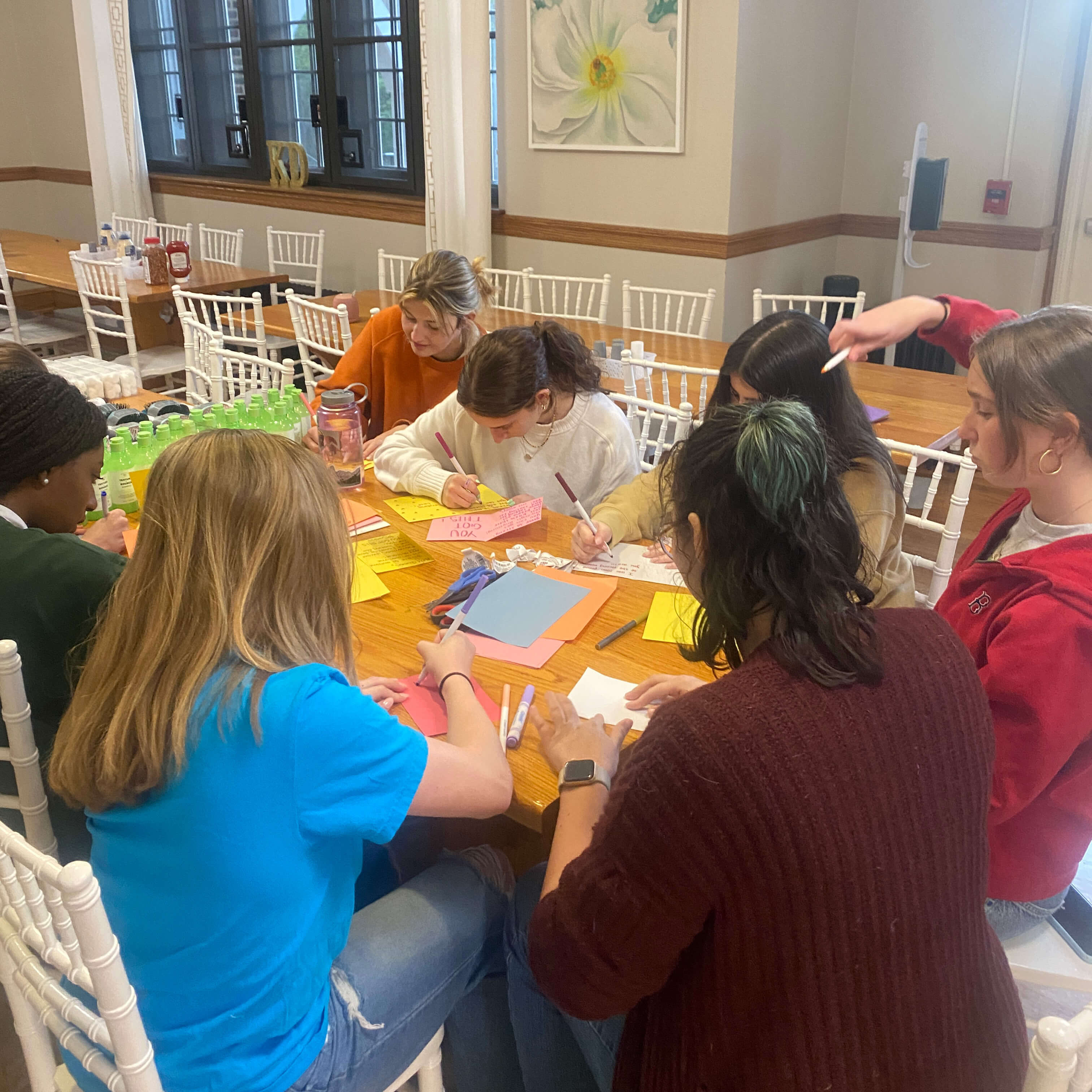 Girl Scouts and Kappa Delta sisters work at a table with heads down creating words of encouragement on colorful paper.