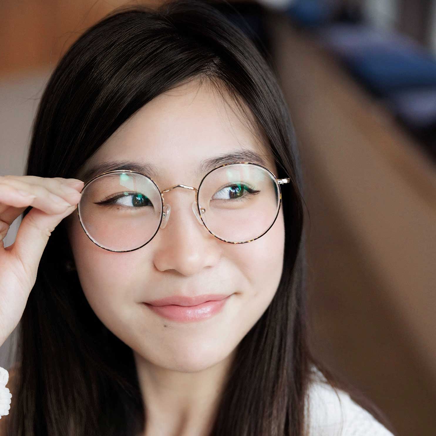 Chen smiles and touches the edge of her glasses. She looks off to the right hand side. Her eyeliner winged and her top is white.