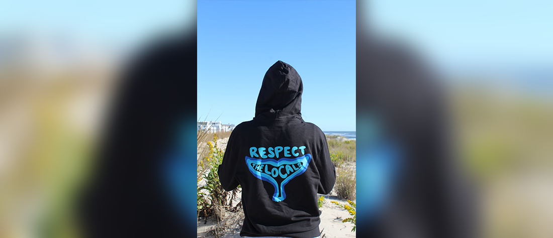 A black hooded sweatshirt that says “Respect the locals” inside the shape of a whale’s tail.